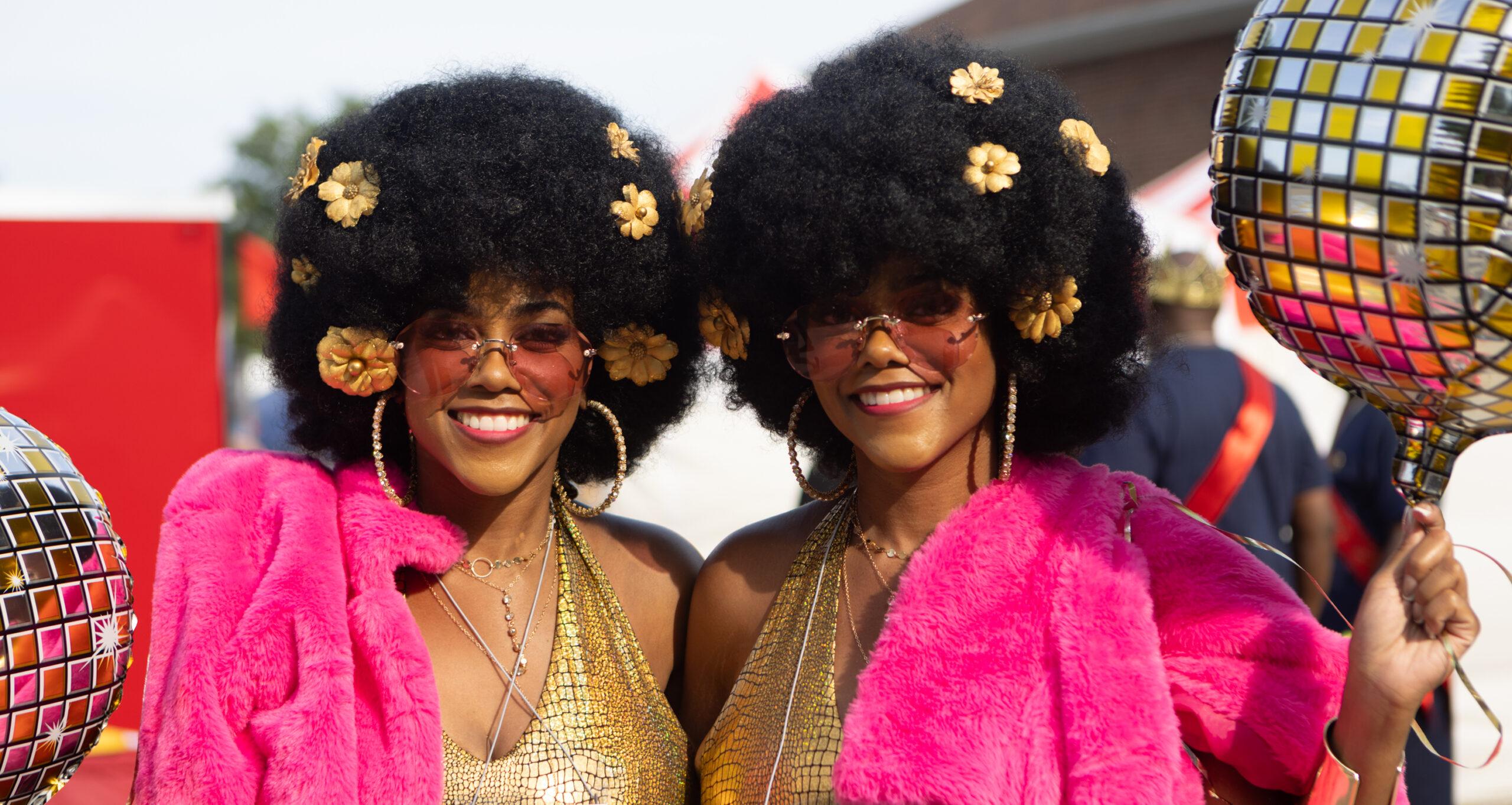 Twin women in ’70s outfits hold balloons decorated as disco balls.