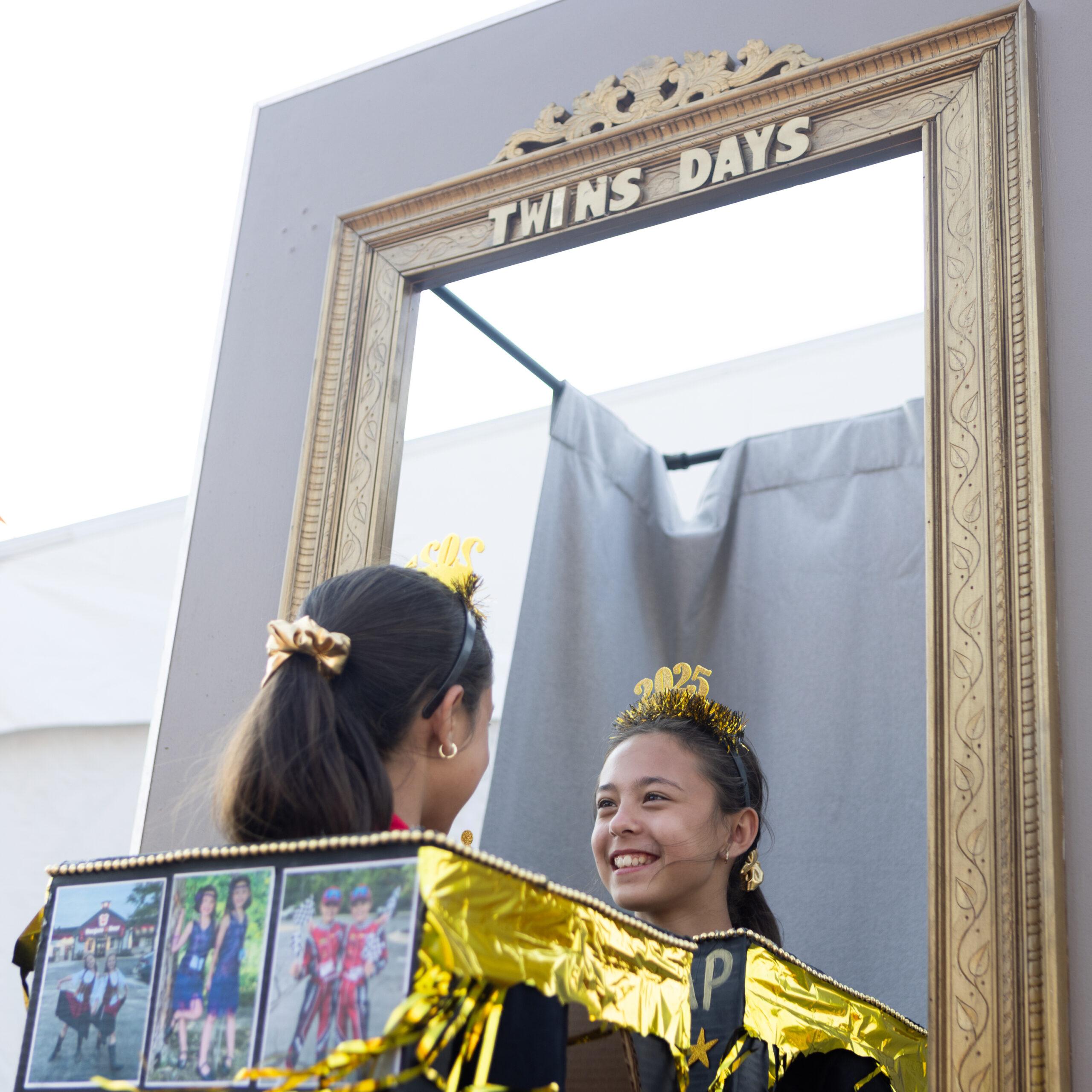 Twin girls are seen on either side of a faux mirror at the Twins Days festival.