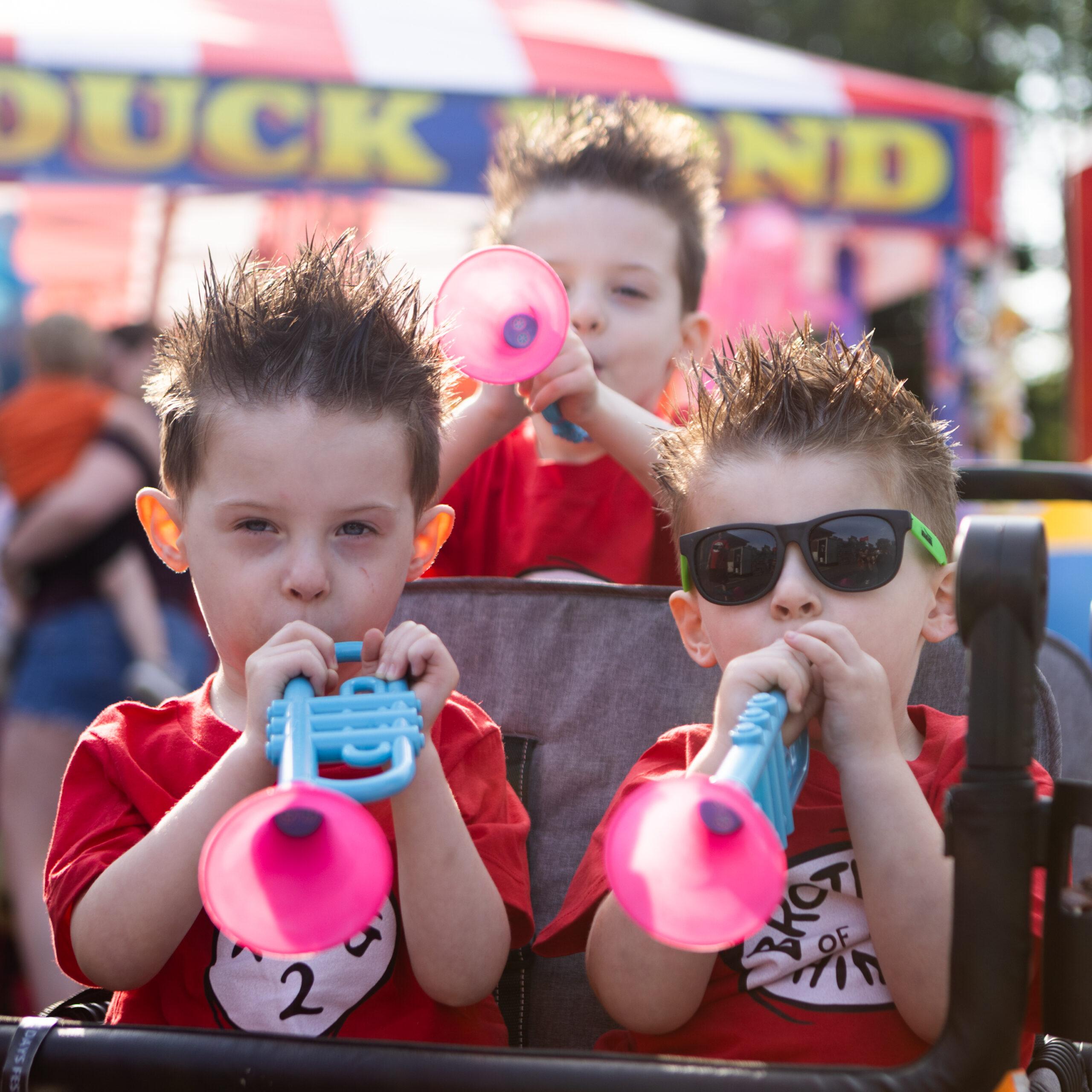 Triplet boys play plastic trumpets at the Twins Days festival.