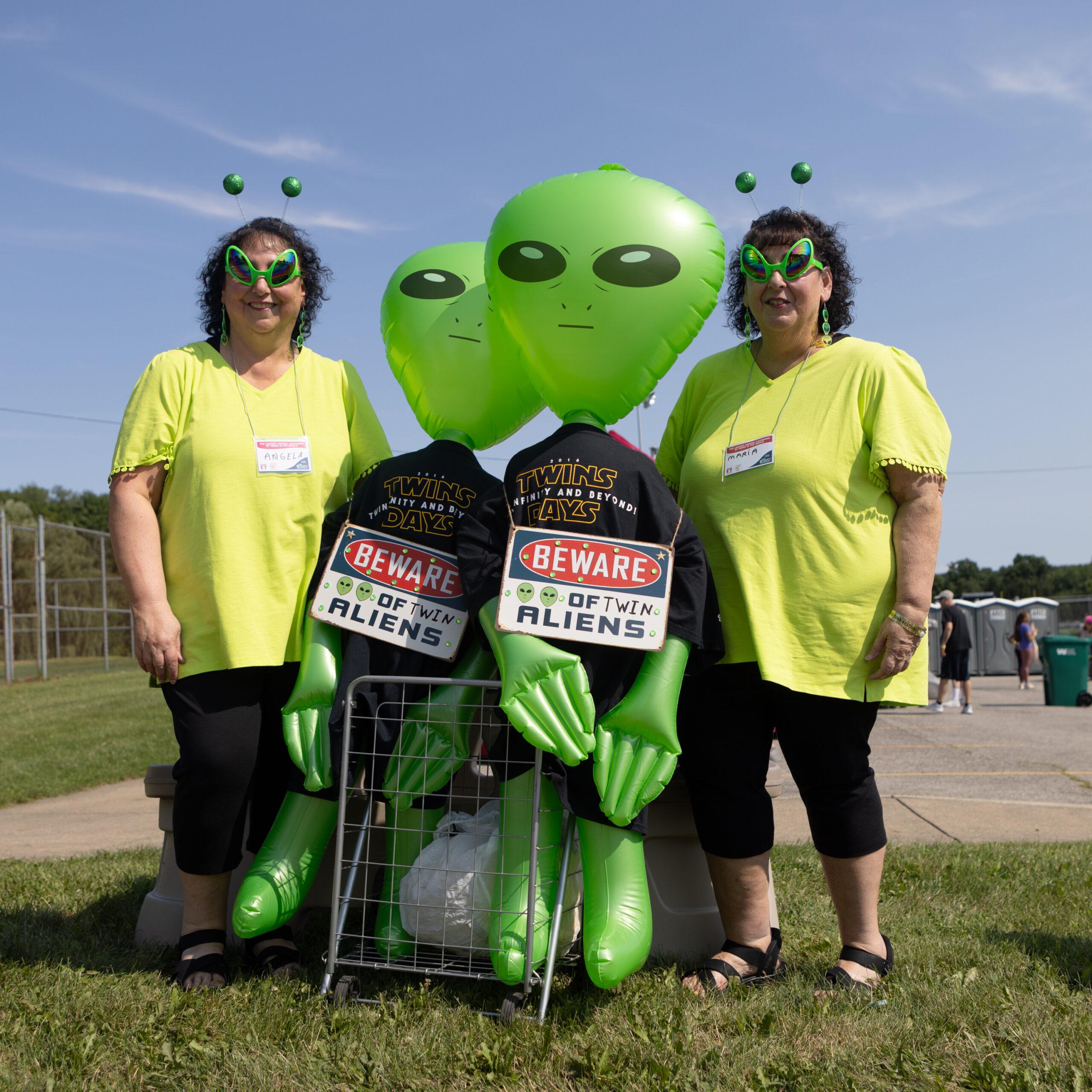 Twin women dressed as aliens pose with inflatable aliens at the Twins Days festival.