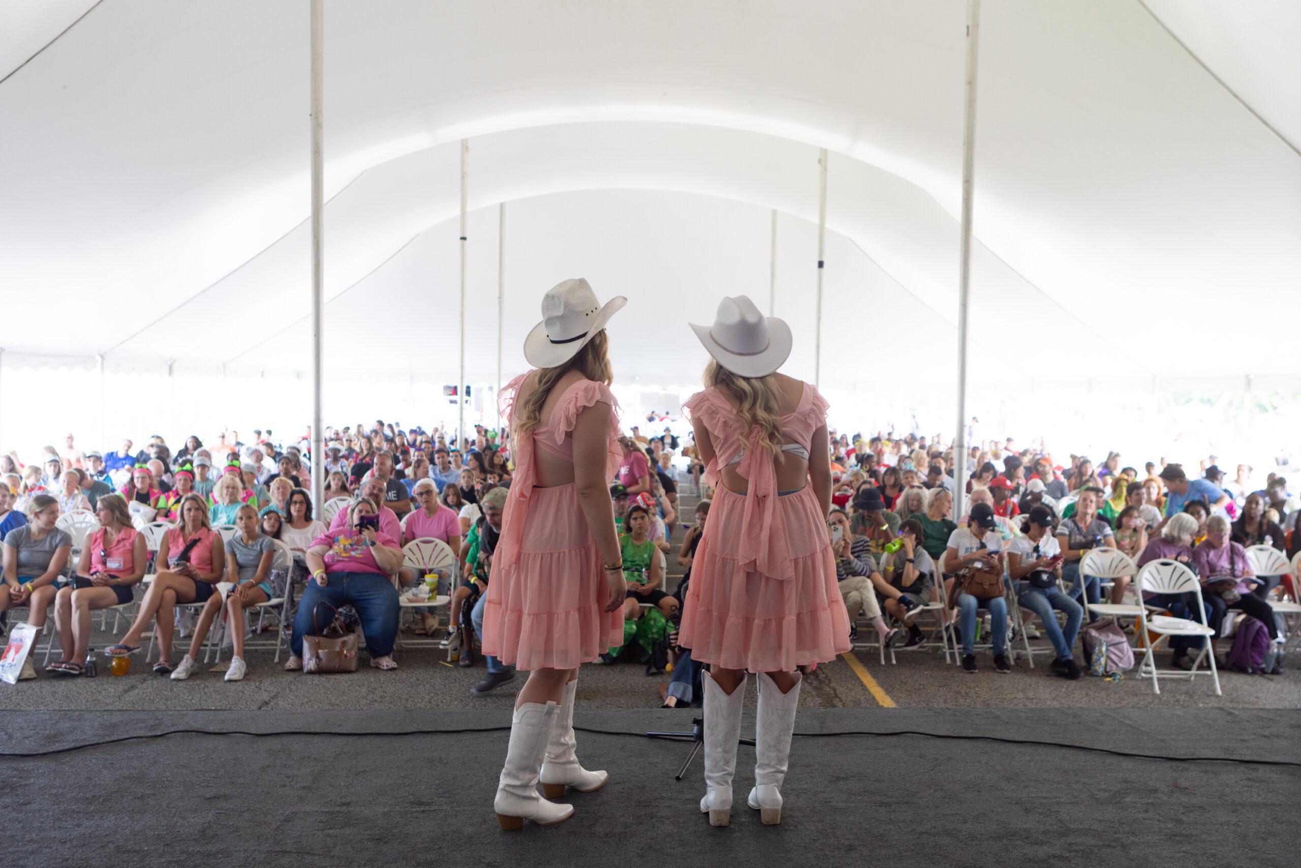 Twin women wearing cowboy hats and boots are seen performing in the talent show at the Twins Days festival.