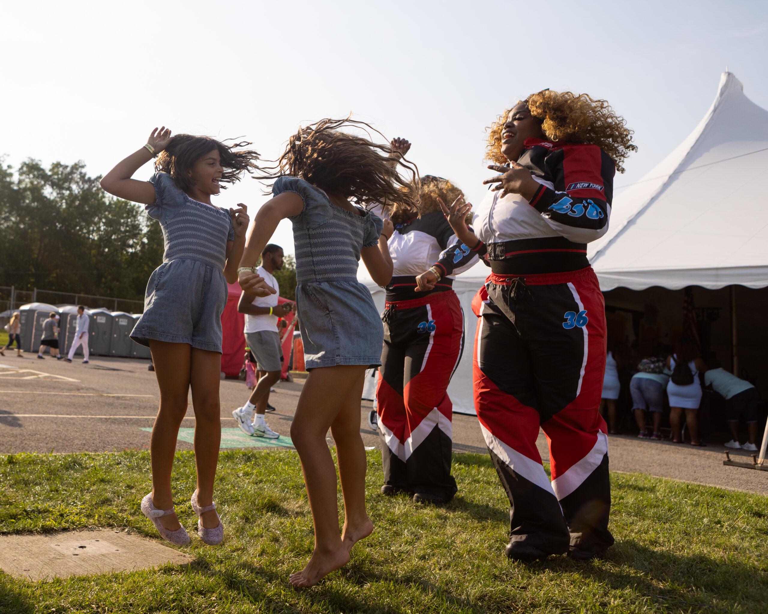 Two sets of female twins — one young, one adult — jump in the air while filming a dance video at the Twins Days festival.
