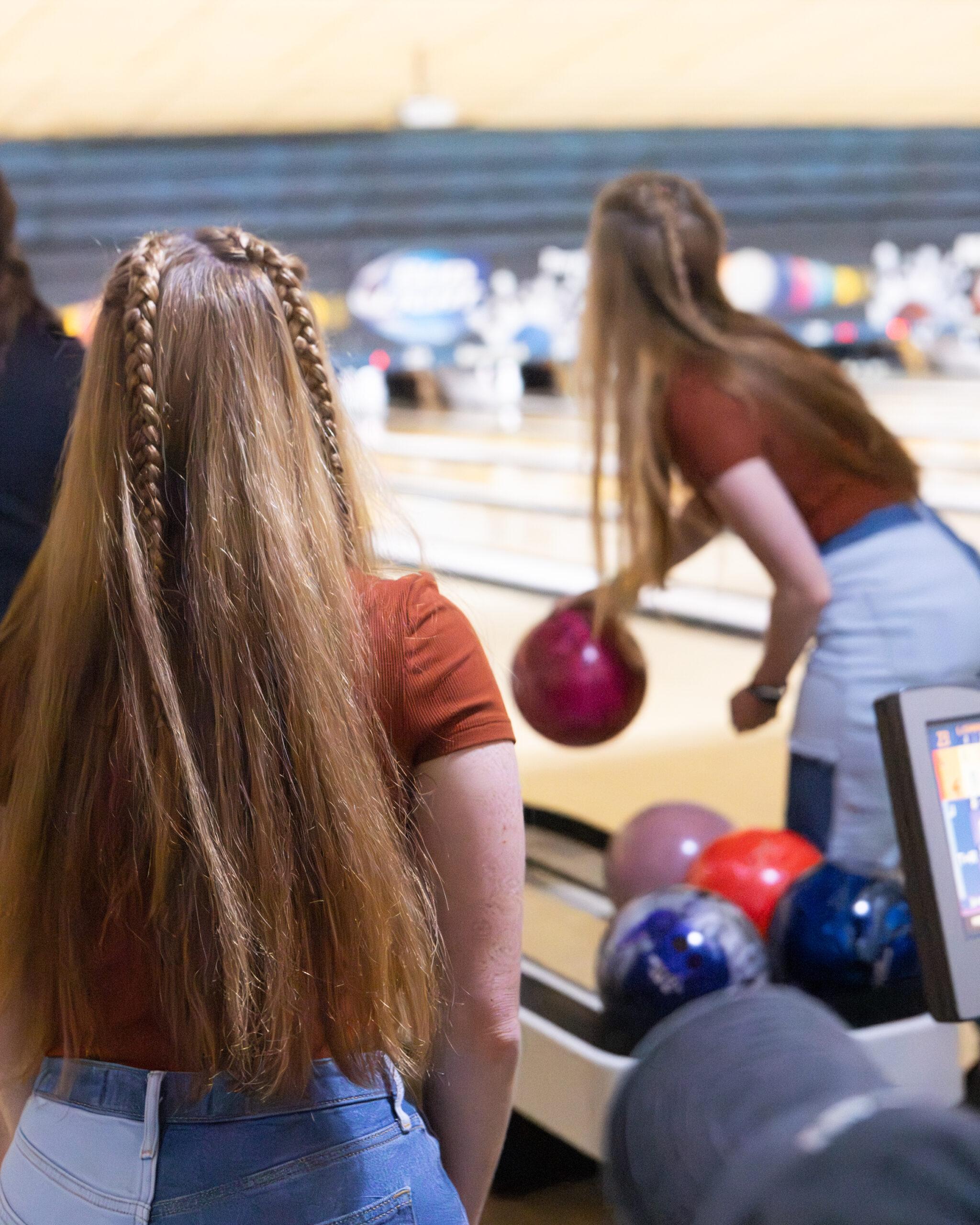 Twin women with matching braids are seen from behind bowling at a bowling alley in Twinsburg.
