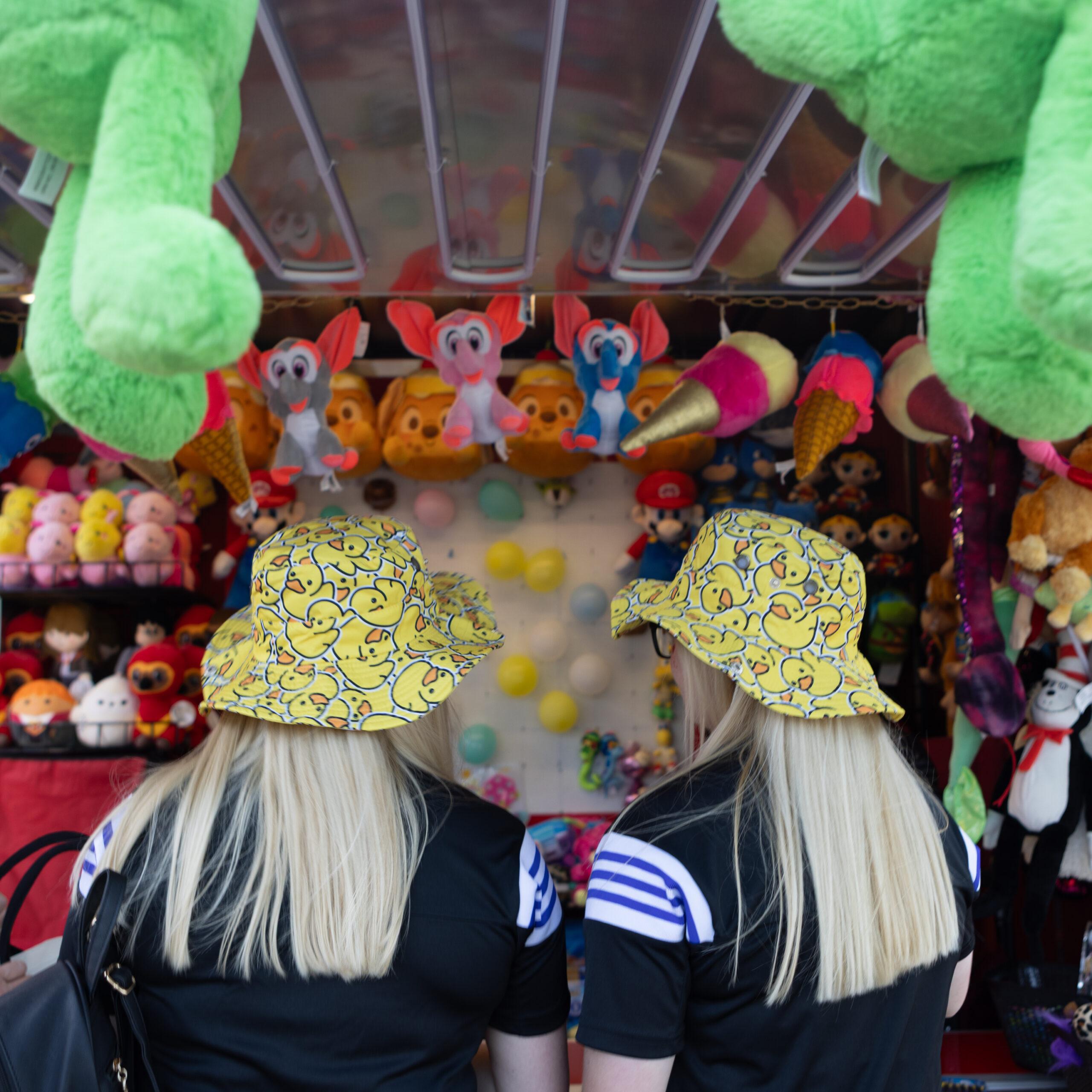 Twin women seen from behind playing a carnival game at the Twins Days festival.