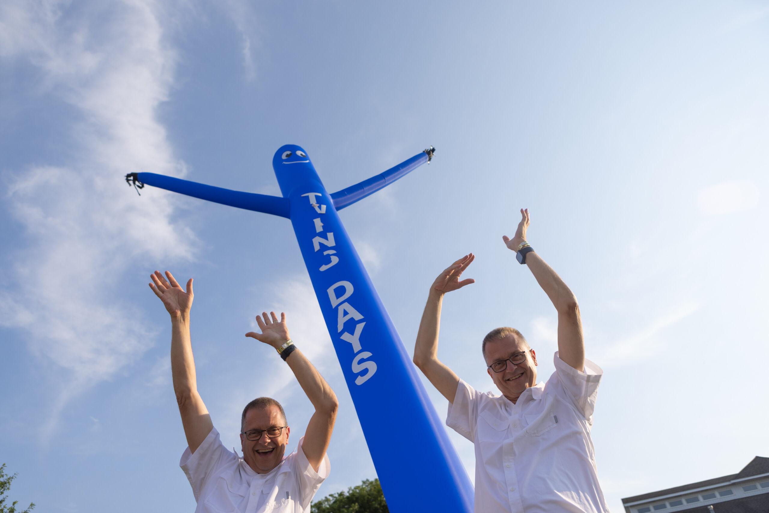 Adult male twins mimic an inflatable man at the Twins Days festival.