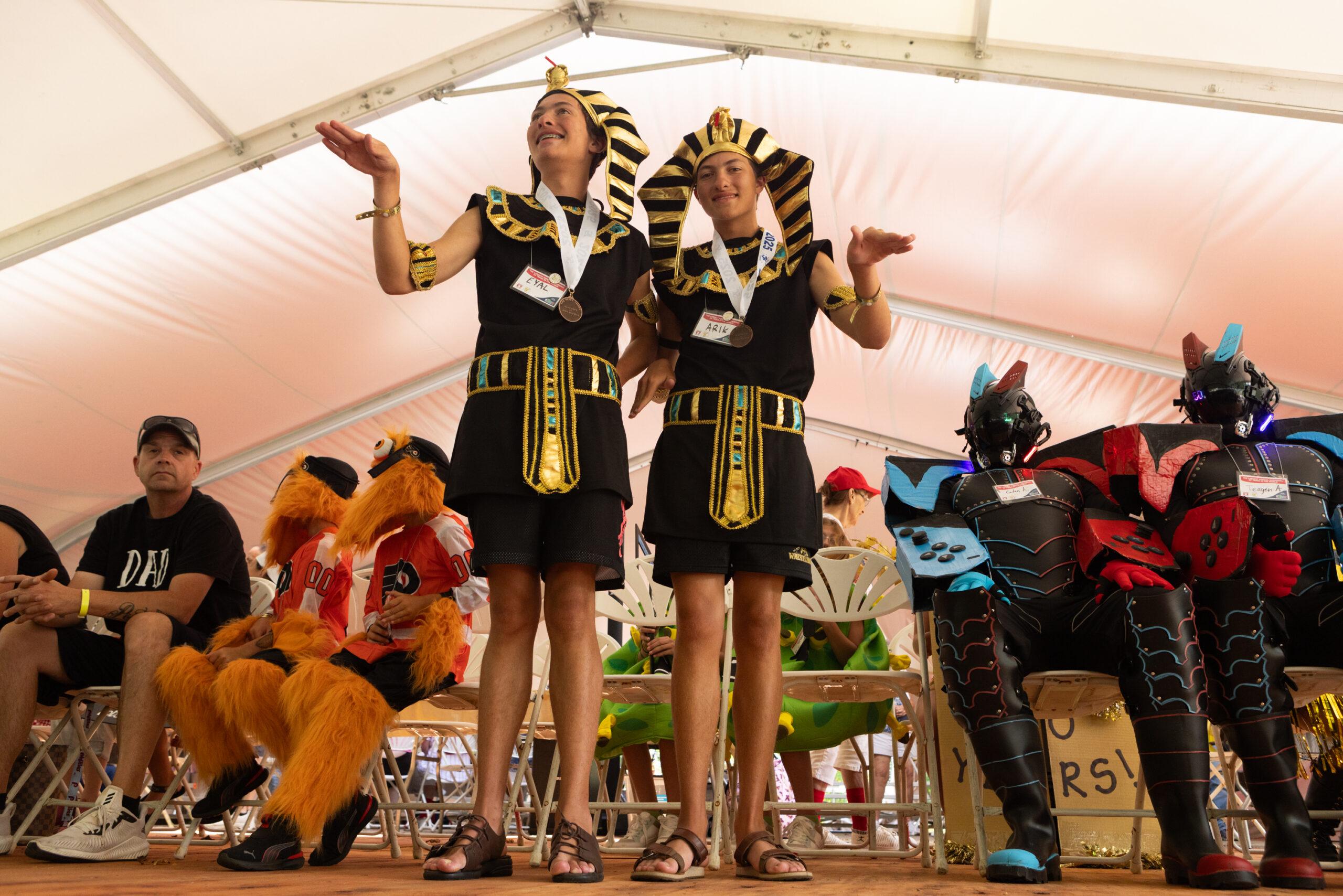 Young male twins dressed as pharaohs pose onstage with other twins in costume at the Twins Days festival.